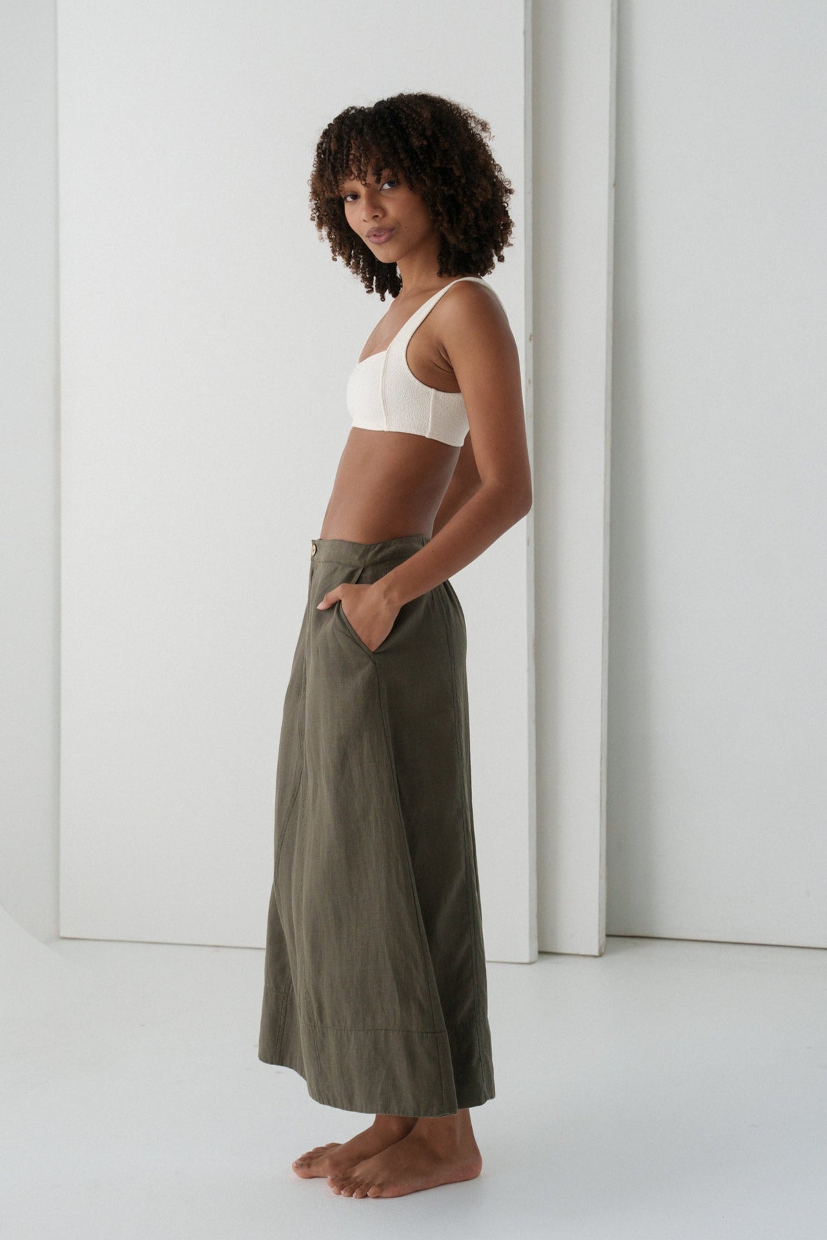 Woman wearing a white bralette and LILLY PILLY Gia linen skirt in Khaki with  a white background