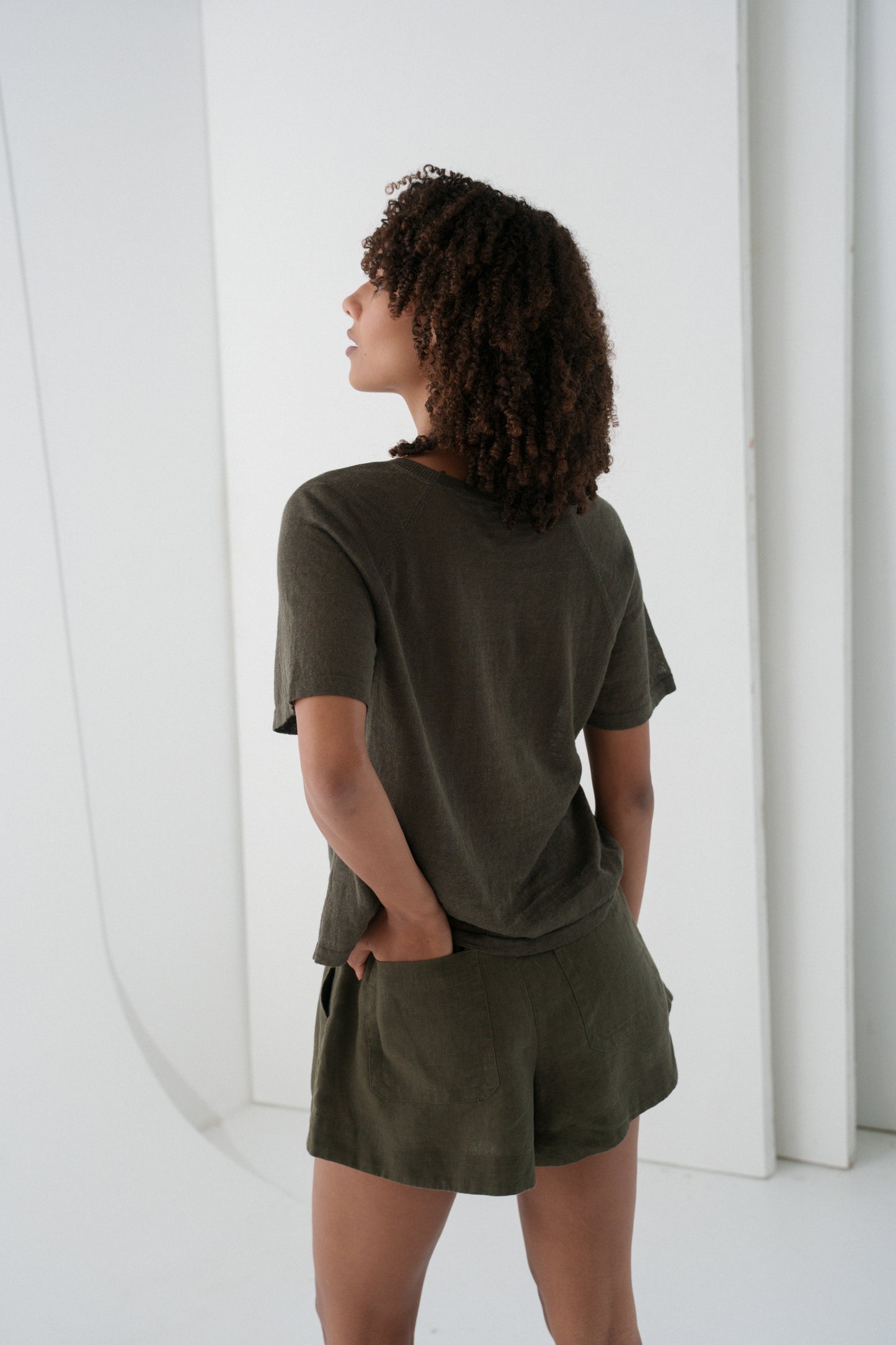 Woman wearing a khaki Grace linen knit top back view with white wall background