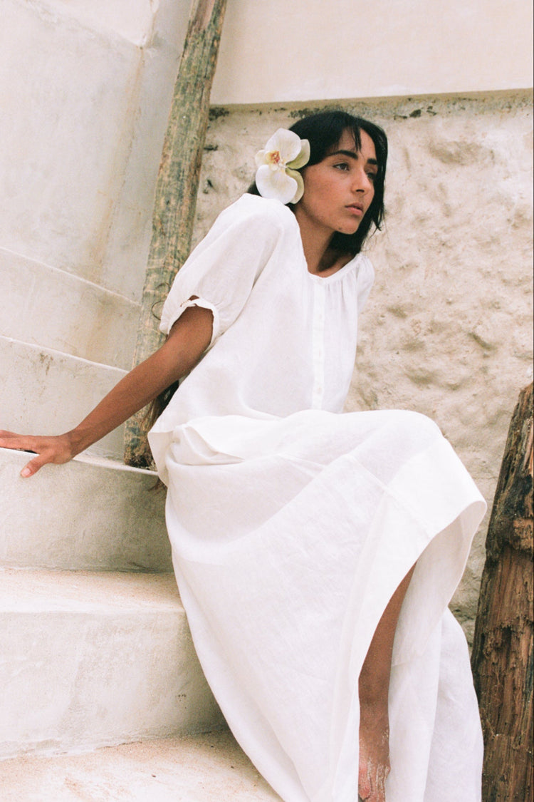 Hannah Linen Maxi Skirt in Ivory - sitting on stone steps, side split, worn with button-front top, coastal stone wall backdrop - Lilly Pilly Collection