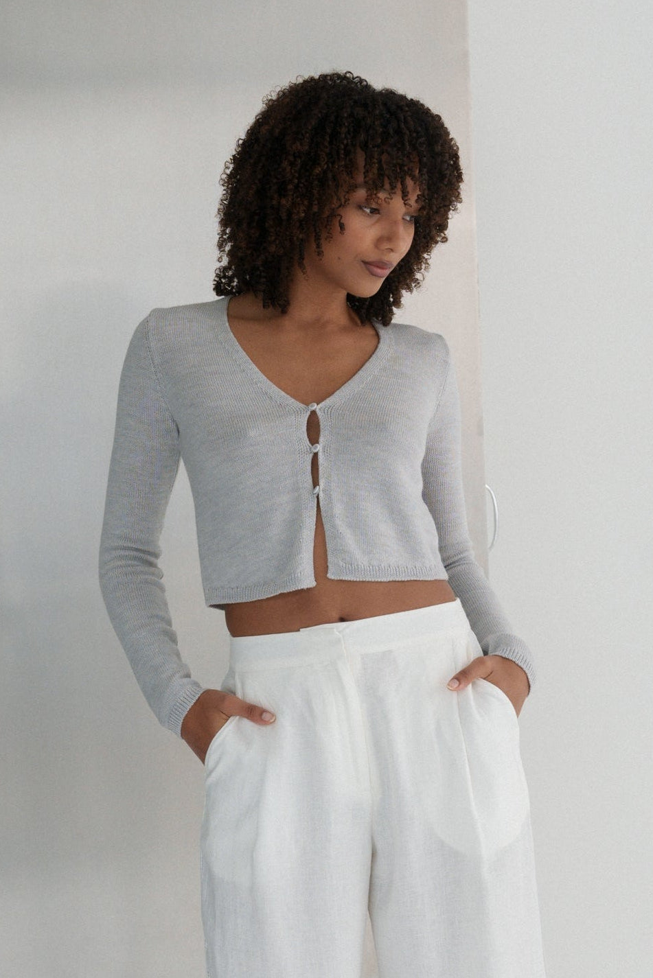LILLY PILLY woman wearing a fog gray Indie merino wool cardigan and ivory Ivy pants against a plain background