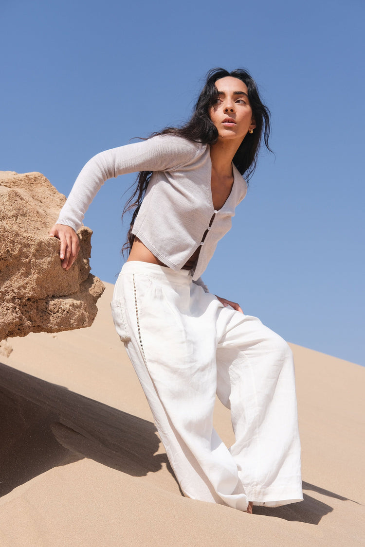 Indie Merino Cardi Knit in Fog Grey - front view, styled with ivory Rika pants, standing on sand under a clear blue sky - Lilly Pilly Collection