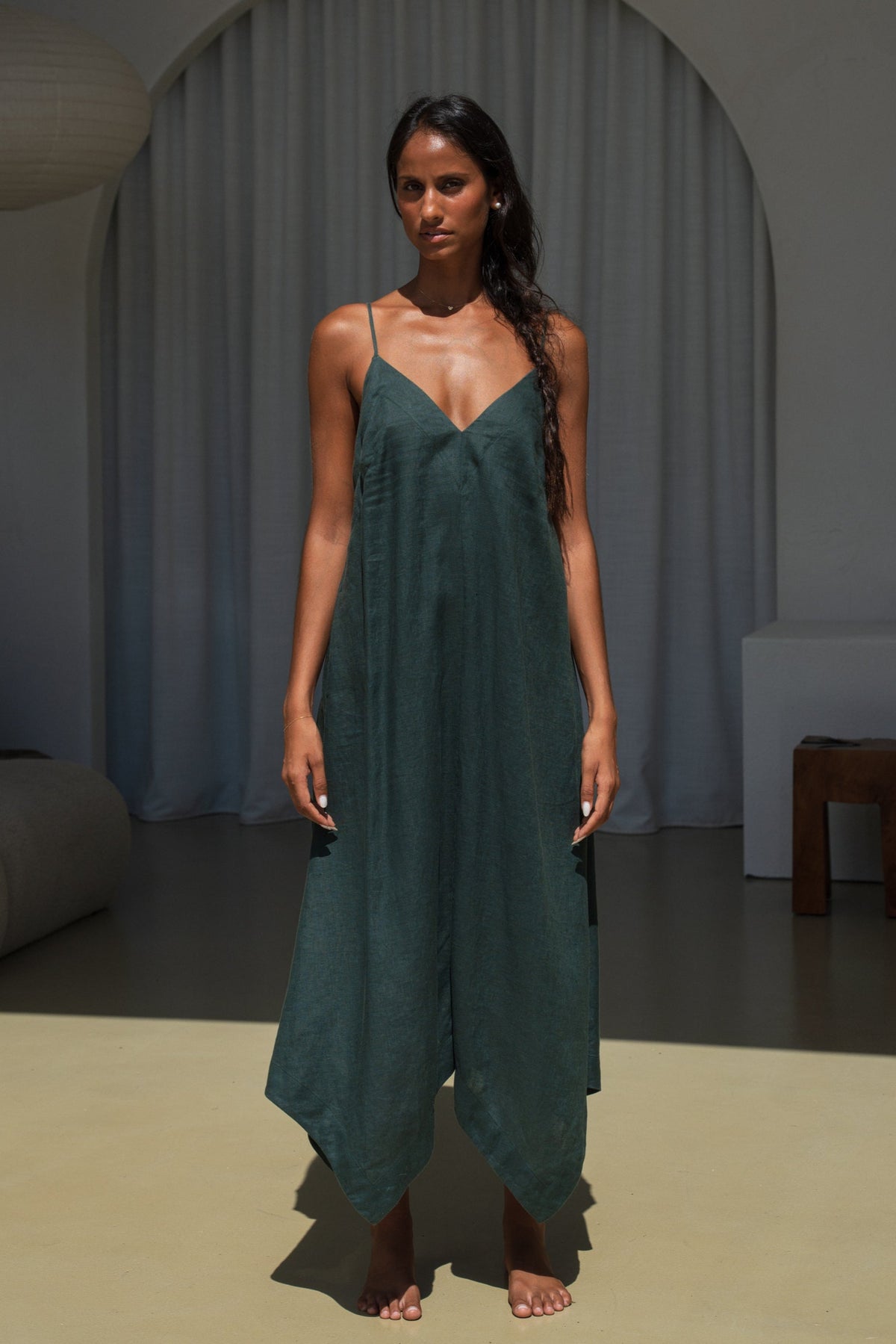 LILLY PILLY woman wearing a forest green Inez linen dress standing in  a minimalistic room with neutral colours.
