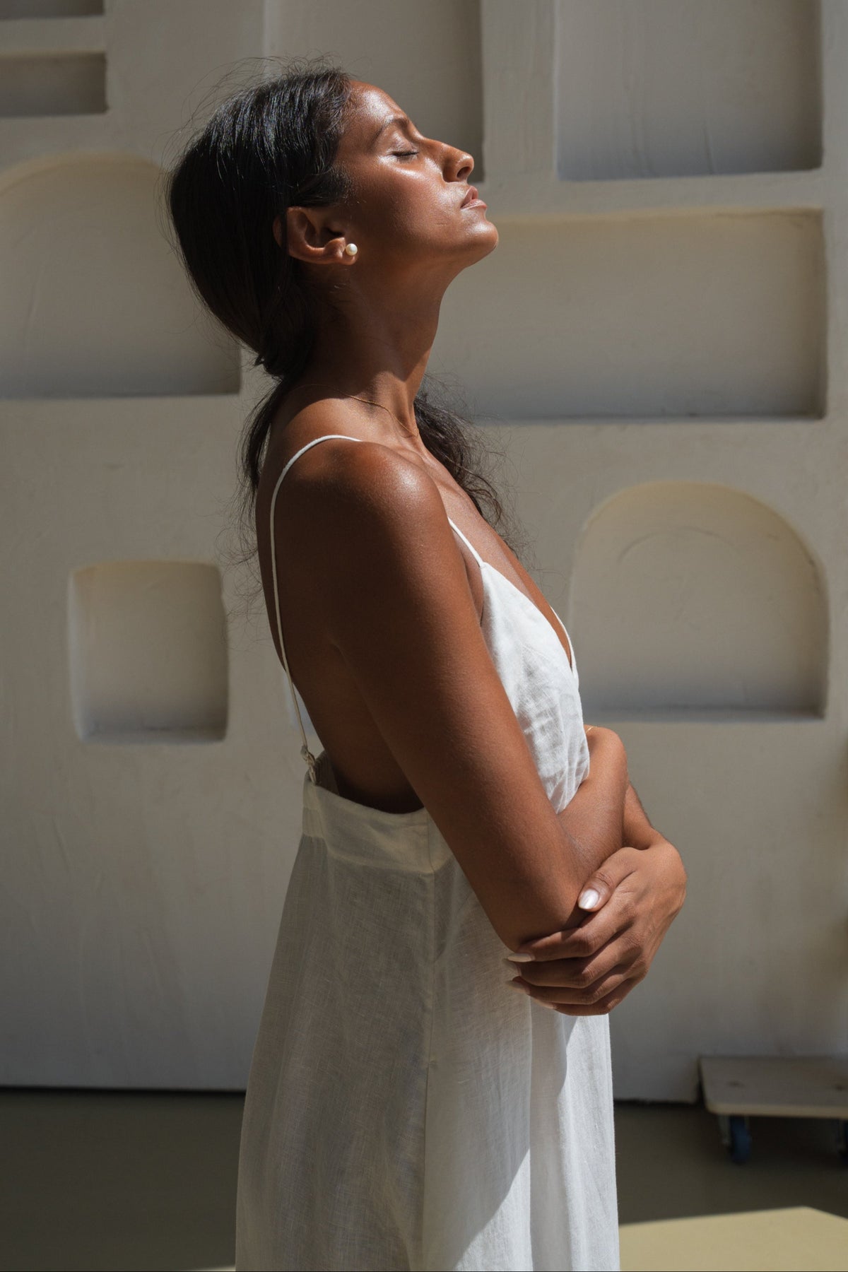 Side view of a woman wearing a ivory white Inez linen dress standing against a light-coloured wall.