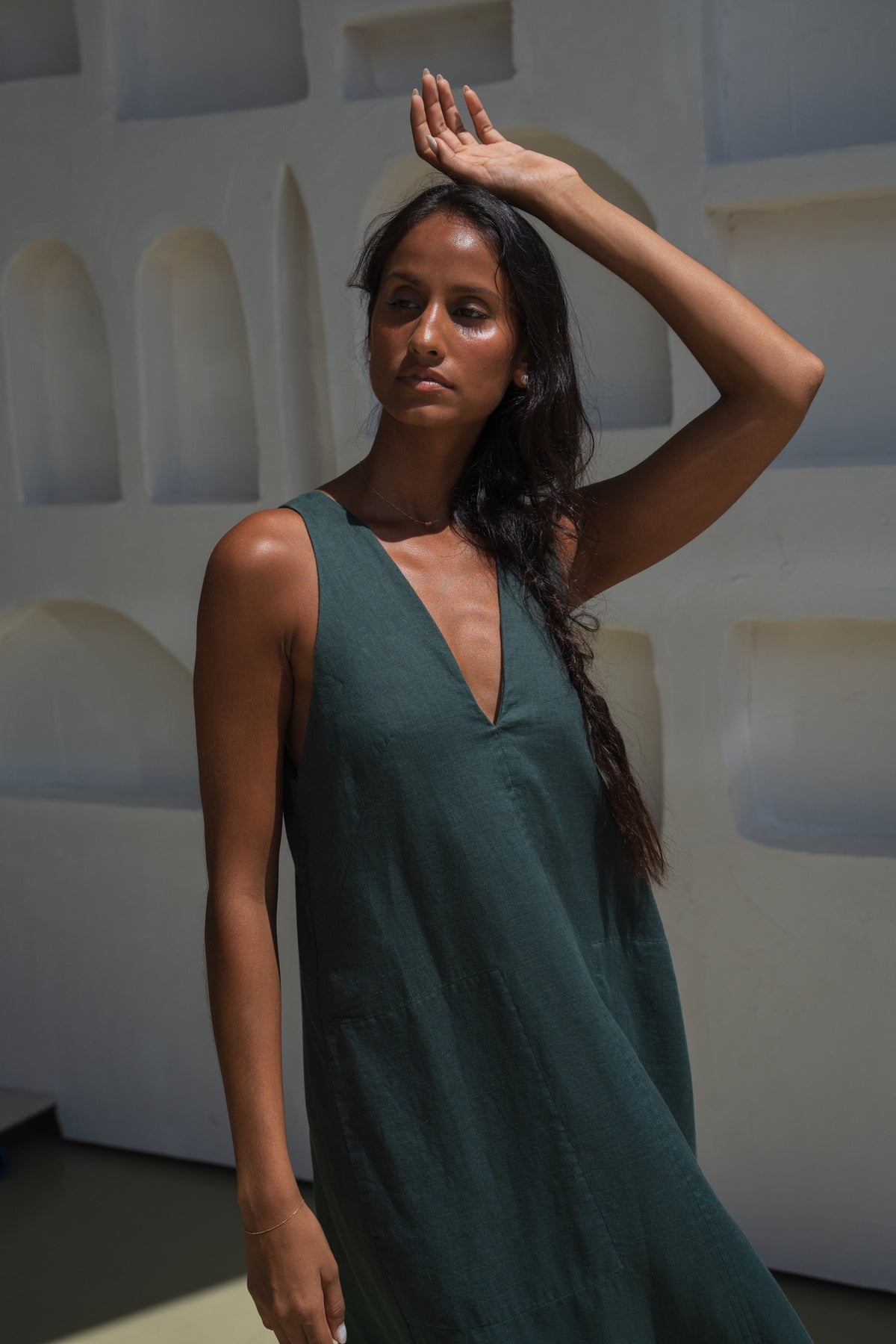 Woman in an forest green LILLY PILLY Iris dress posing against a white wall with geometric shapes with her hand on head