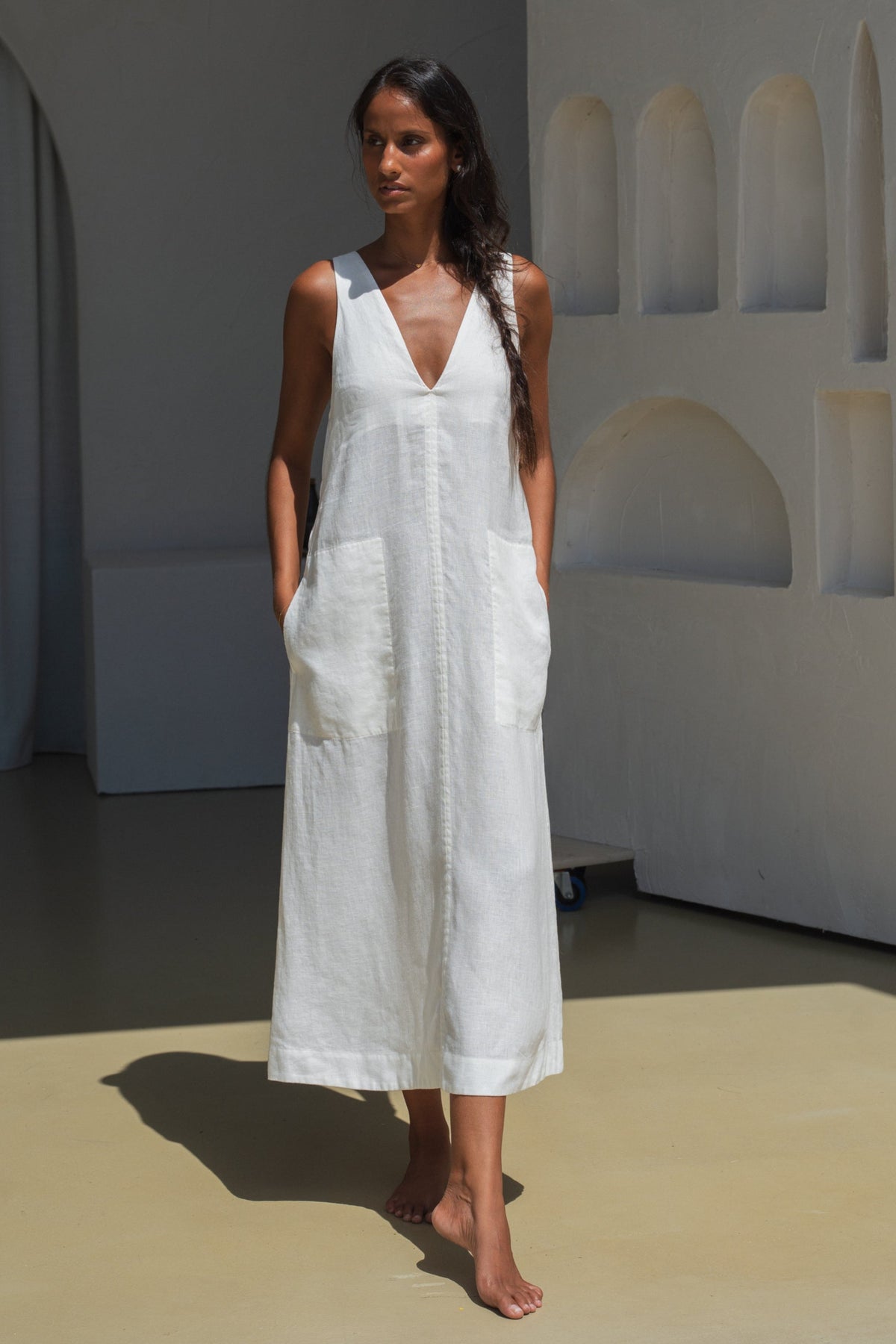LILLY PILLY woman wearing an ivory white Iris dress standing in a minimalistic room with architectural wall design.