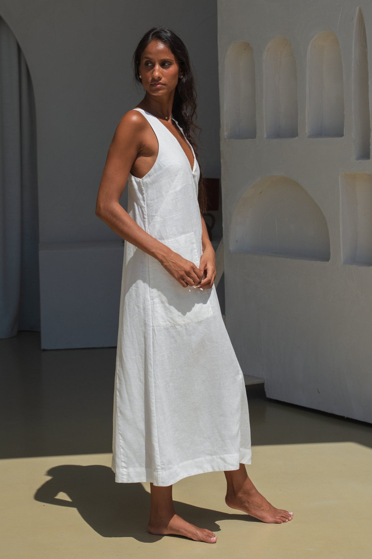 LILLY PILLY woman showing the side view of an ivory white Iris dress standing against a minimalistic background