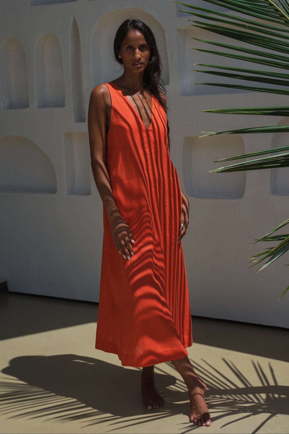 LILLY PILLY woman wearing a spritz Iris dress with a plant in the background against a white wall with greenery
