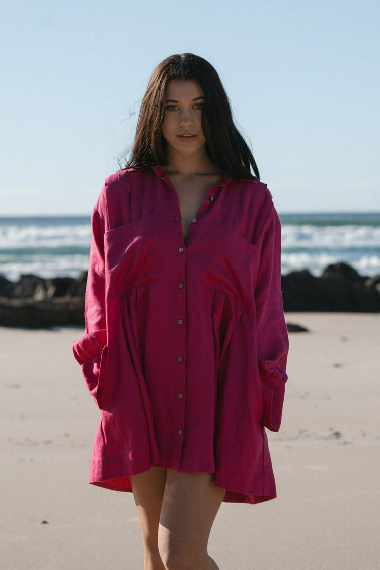 Isabella Linen Shirt Dress in Fuchsia Pink - front view, collared button-front, gathered waist yoke, standing on beach with ocean and rocks backdrop - Lilly Pilly Collection