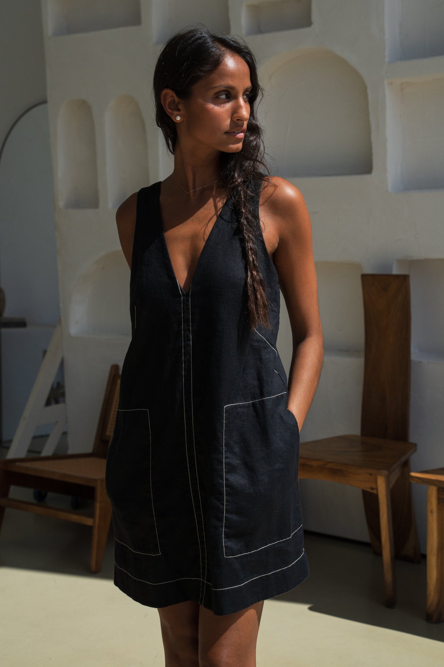 LILLY PILLY woman in an black Isla linen dress with white stitching posing with hands in pockets in an indoor setting