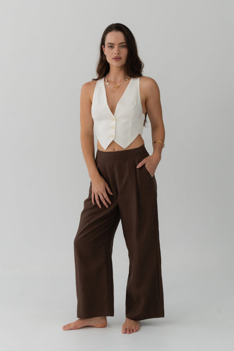 Ivy Linen Crop Pants in Chocolate - full length front view, woman wearing Chocolate wide-leg linen pants with ivory linen waistcoat, hand in pocket, studio backdrop - Lilly Pilly Collection