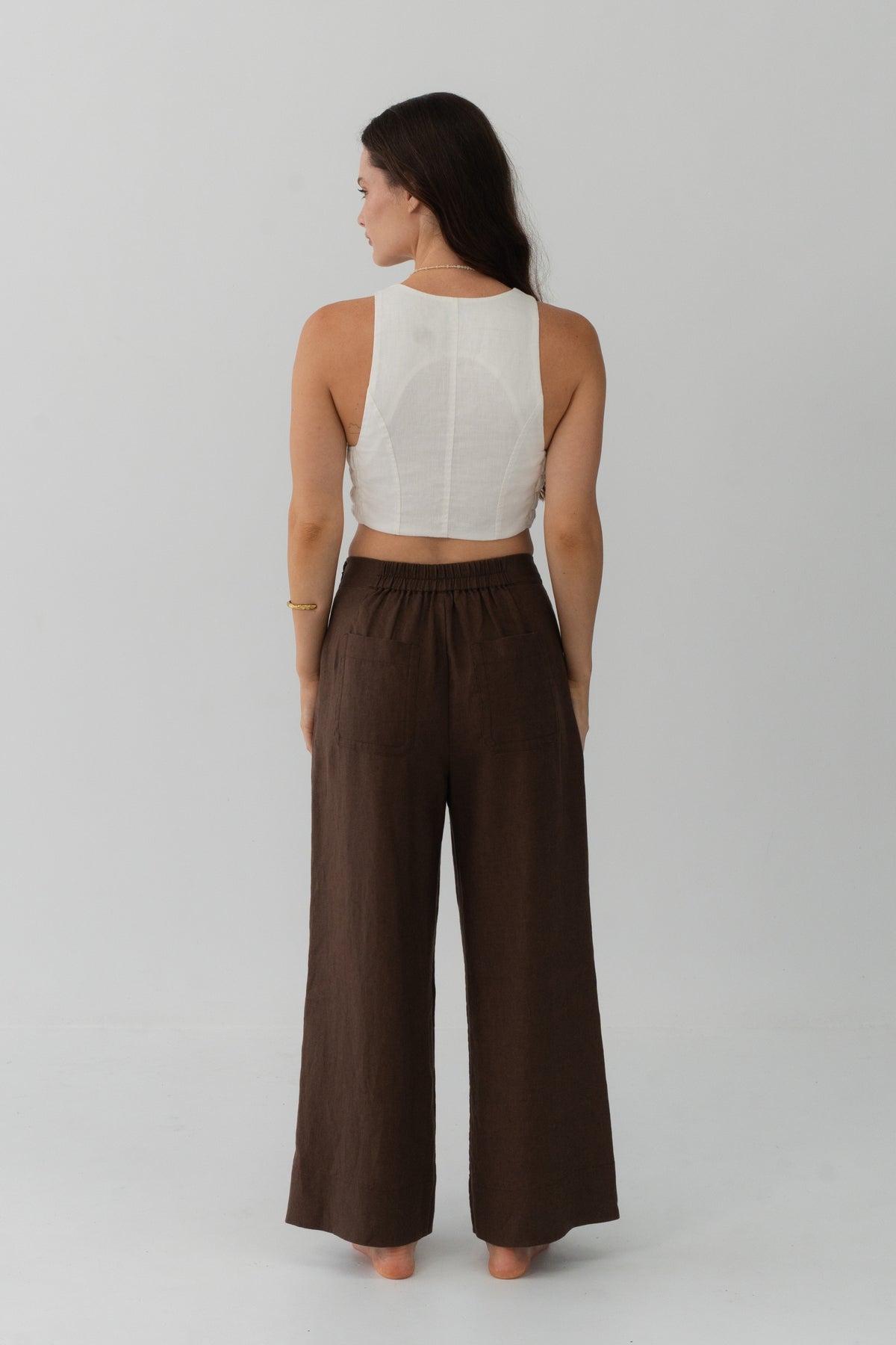 Ivy Linen Crop Pants in Chocolate - back view, woman wearing Chocolate wide-leg linen pants with ivory crop top, elasticated waistband detail, studio backdrop - Lilly Pilly Collection