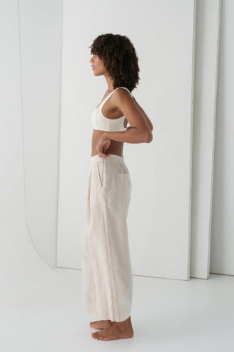 Ivy Linen Crop Pants in Oatmeal - side view showing front pleat and wide-leg linen crop silhouette, woman wearing ivory square-neck crop bra top, white studio backdrop - Lilly Pilly Collection