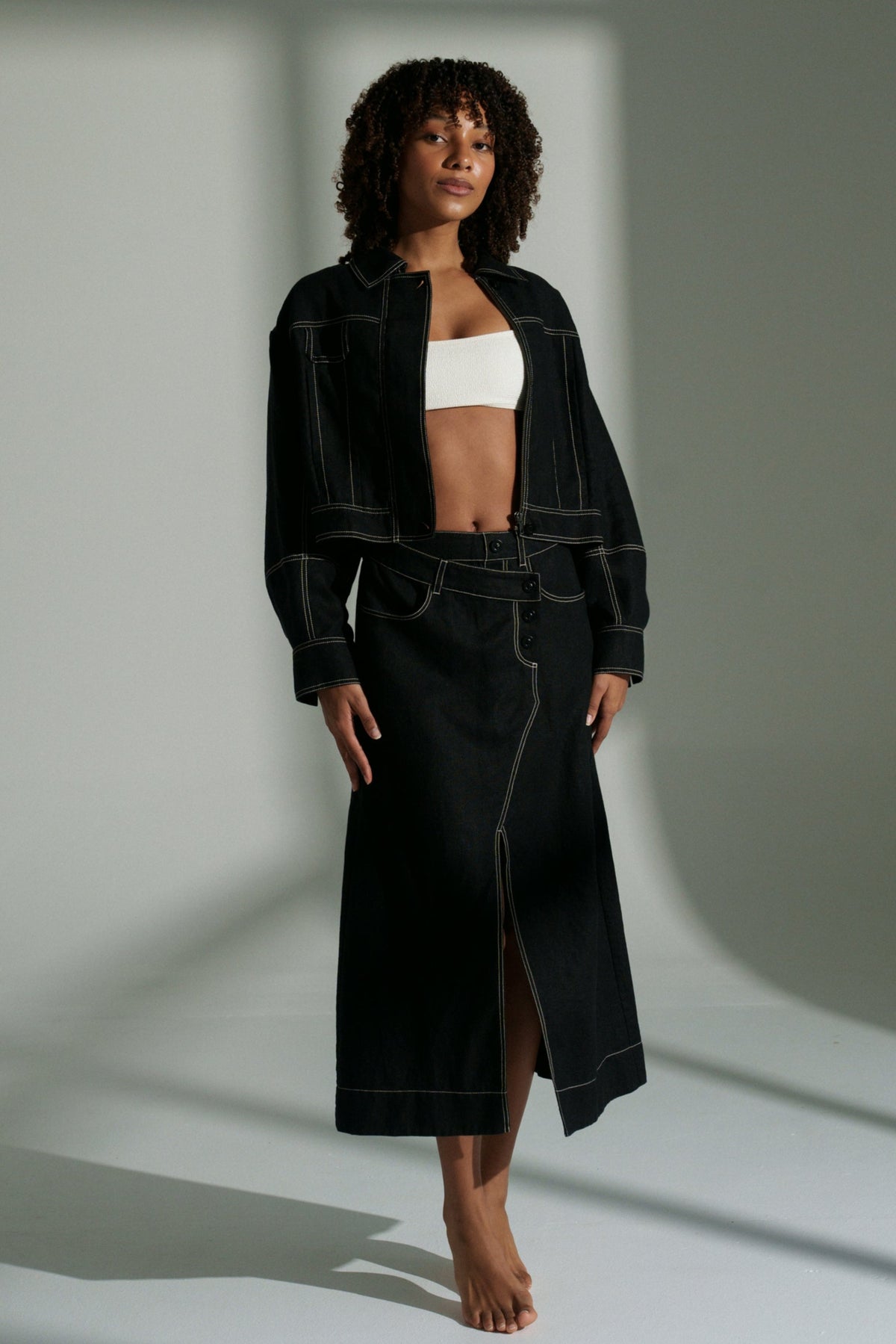 LILLY PILLY woman wearing a black Wes linen jacket and Jax linen skirt outfit with a white top against a neutral background