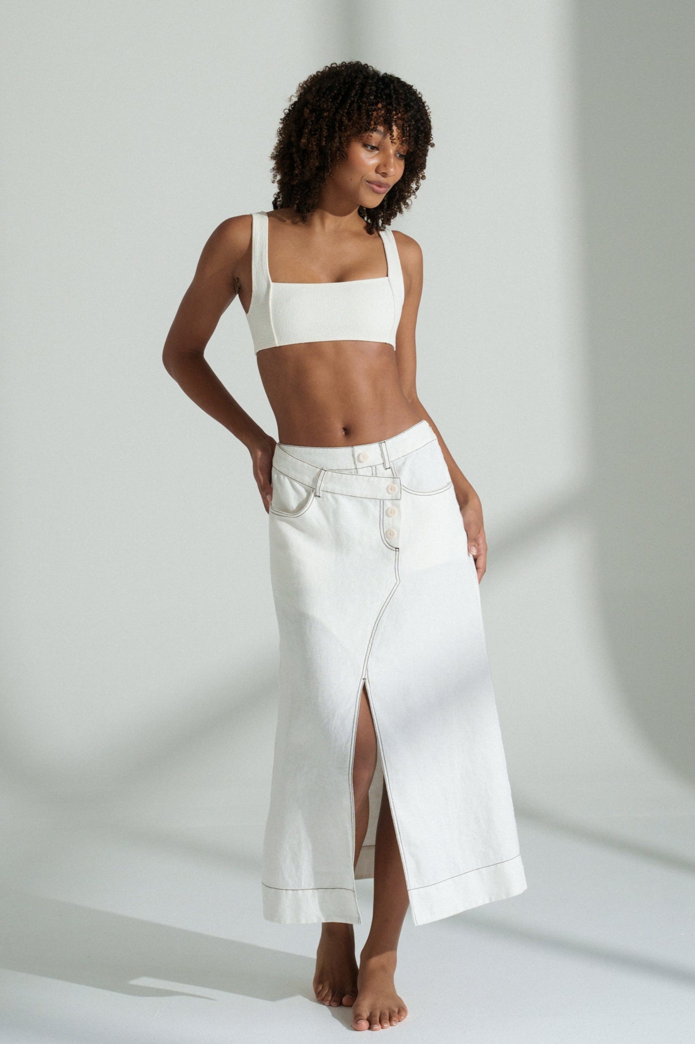 LILLY PILLY woman in a ivory Jax Skirt standing in a minimalistic setting with light casting shadows.