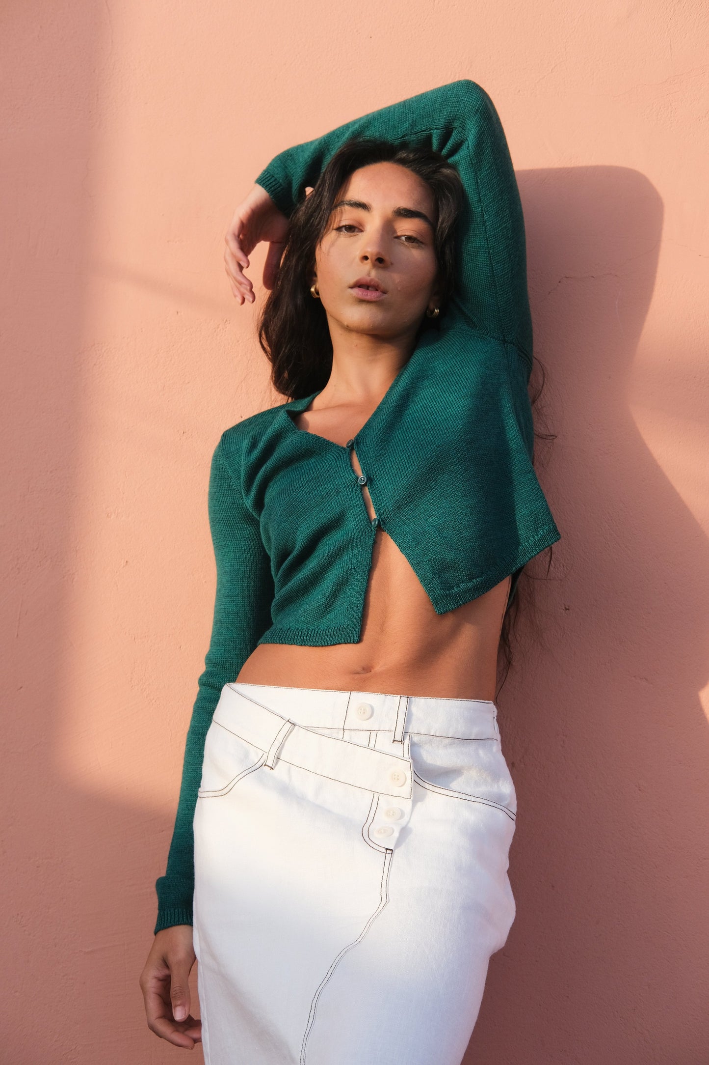 LILLY PILLY woman in a ivory Jax Skirt and a forest green cropped Indie merino cardi against a pink wall