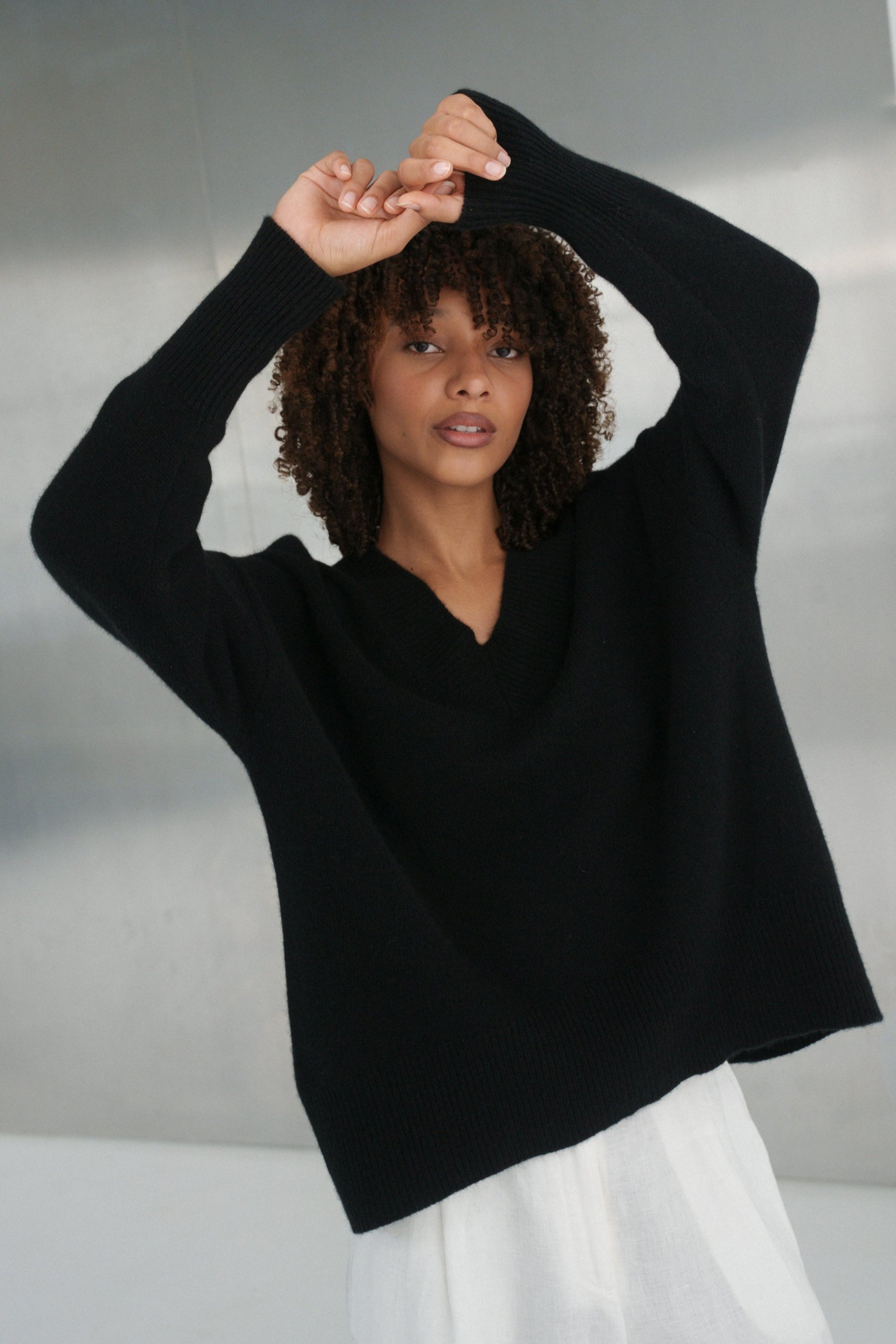 LILLY PILLY woman wearing an black June cashmere knit and ivory linen pants in a minimalistic setting