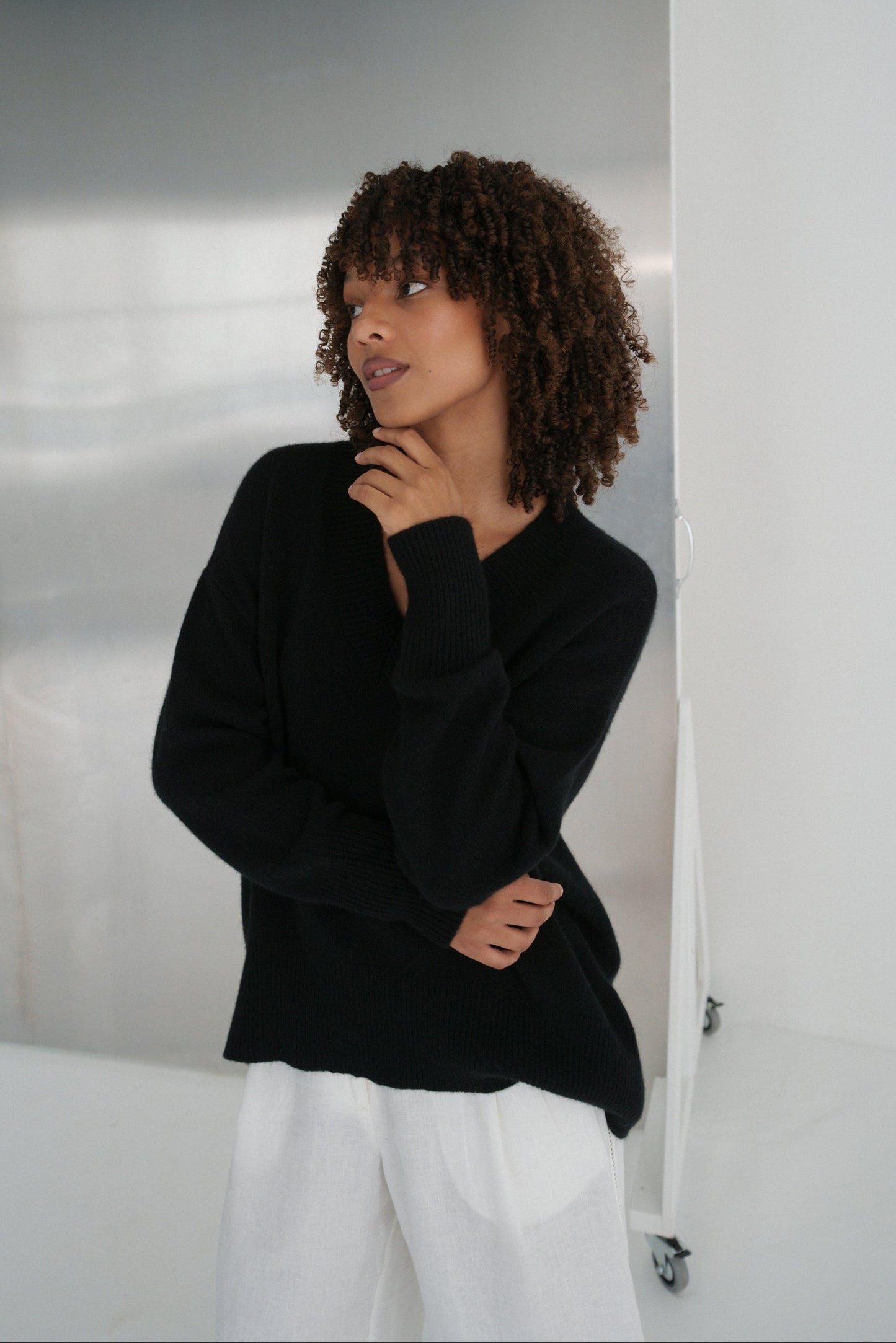 LILLY PILLY woman wearing an black June cashmere knit and ivory linen pants with arms crossed standing against a neutral background