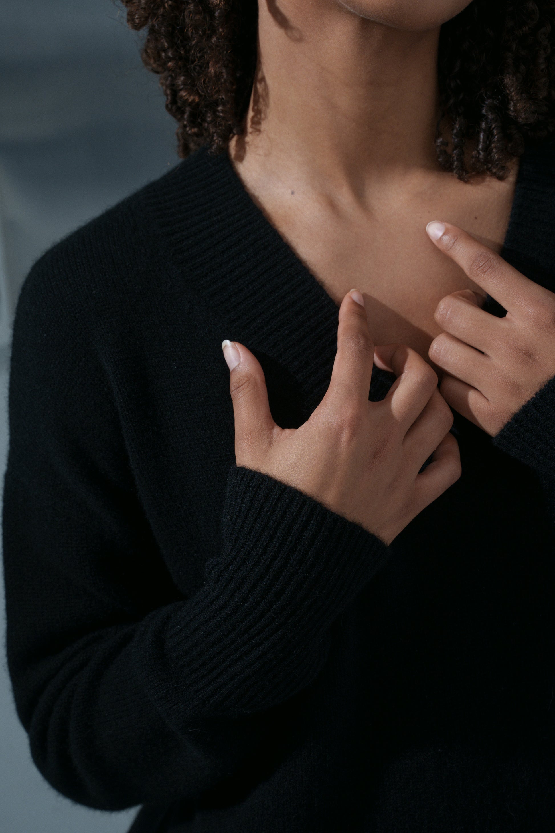 LILLY PILLY woman wearing an black June cashmere knit and ivory linen pants with hands adjusting the neckline