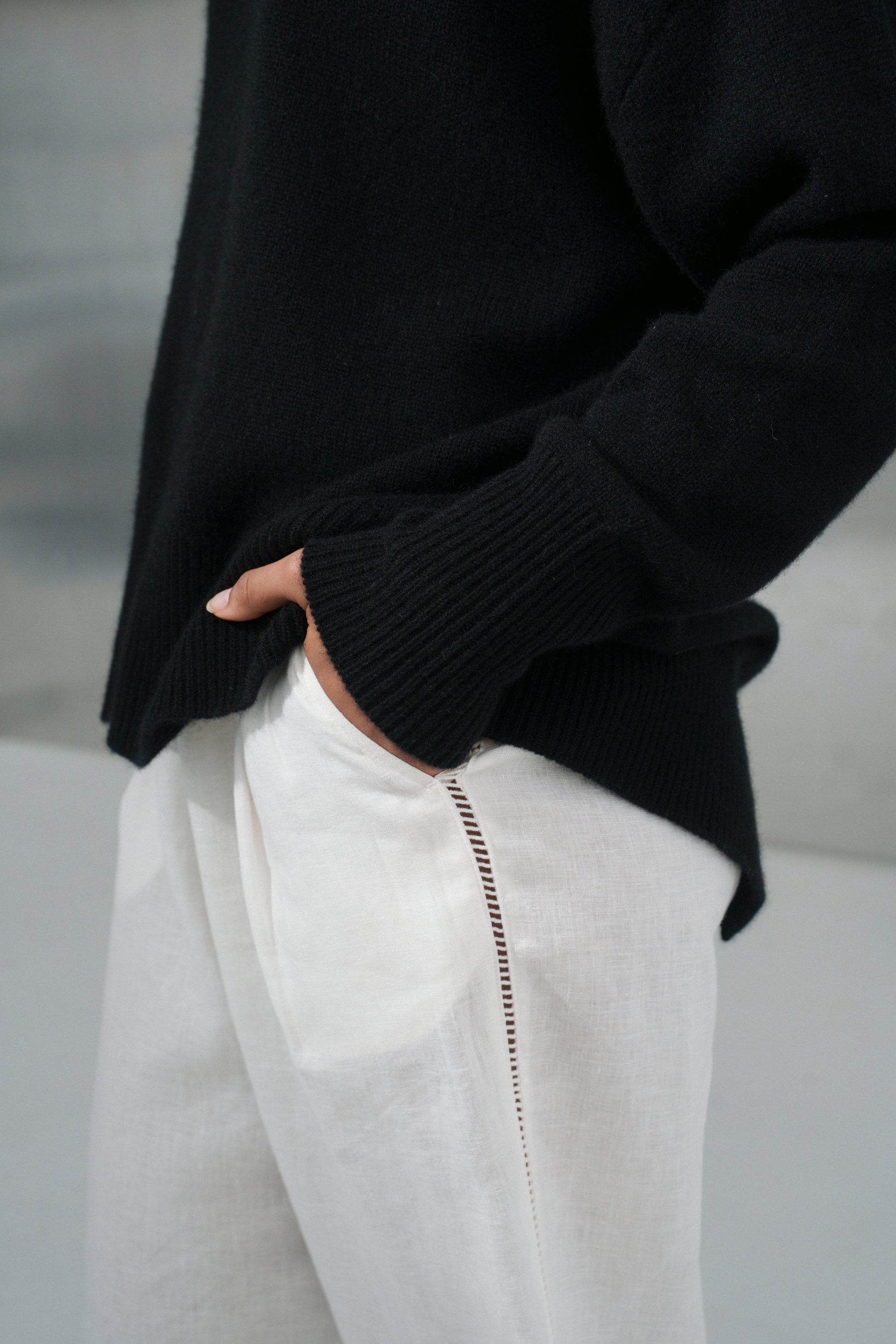 LILLY PILLY woman wearing an black June cashmere knit and ivory linen pants showing sleeve close up view