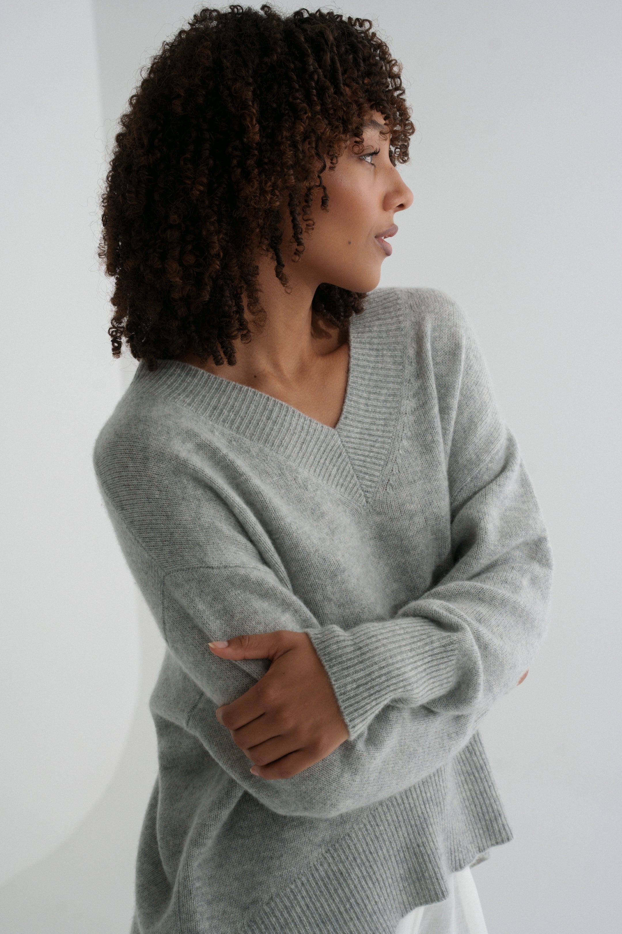 LILLY PILLY woman wearing a grey marle June cashmere knit sweater and ivory linen pants against a white background with arms folded