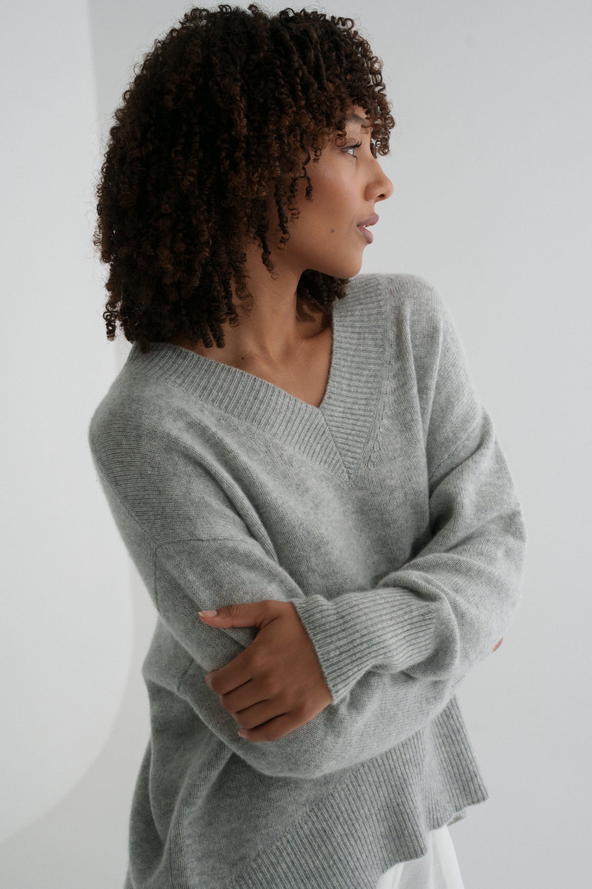LILLY PILLY woman wearing a grey marle June cashmere knit sweater and ivory linen pants against a white background with arms folded