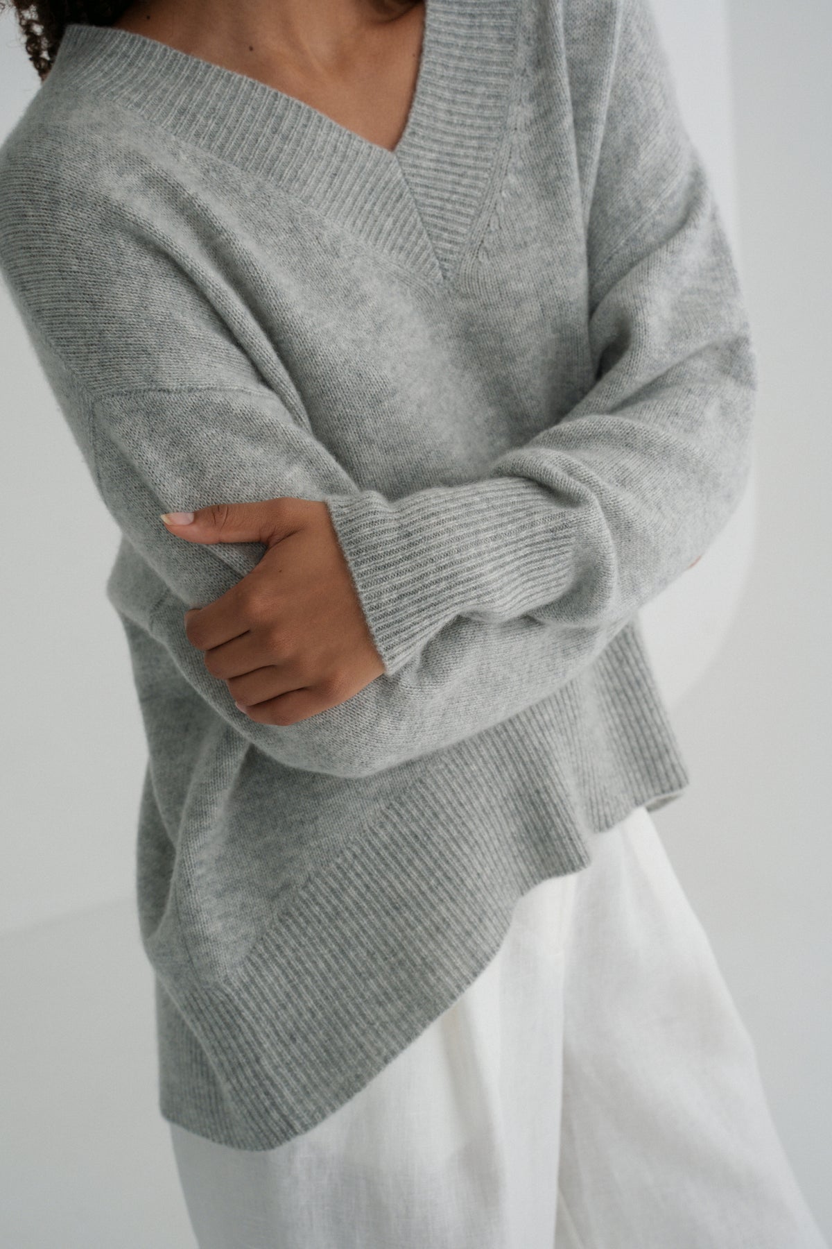Close up view of LILLY PILLY woman wearing a grey marle June cashmere knit sweater and ivory linen pants with a plain white background