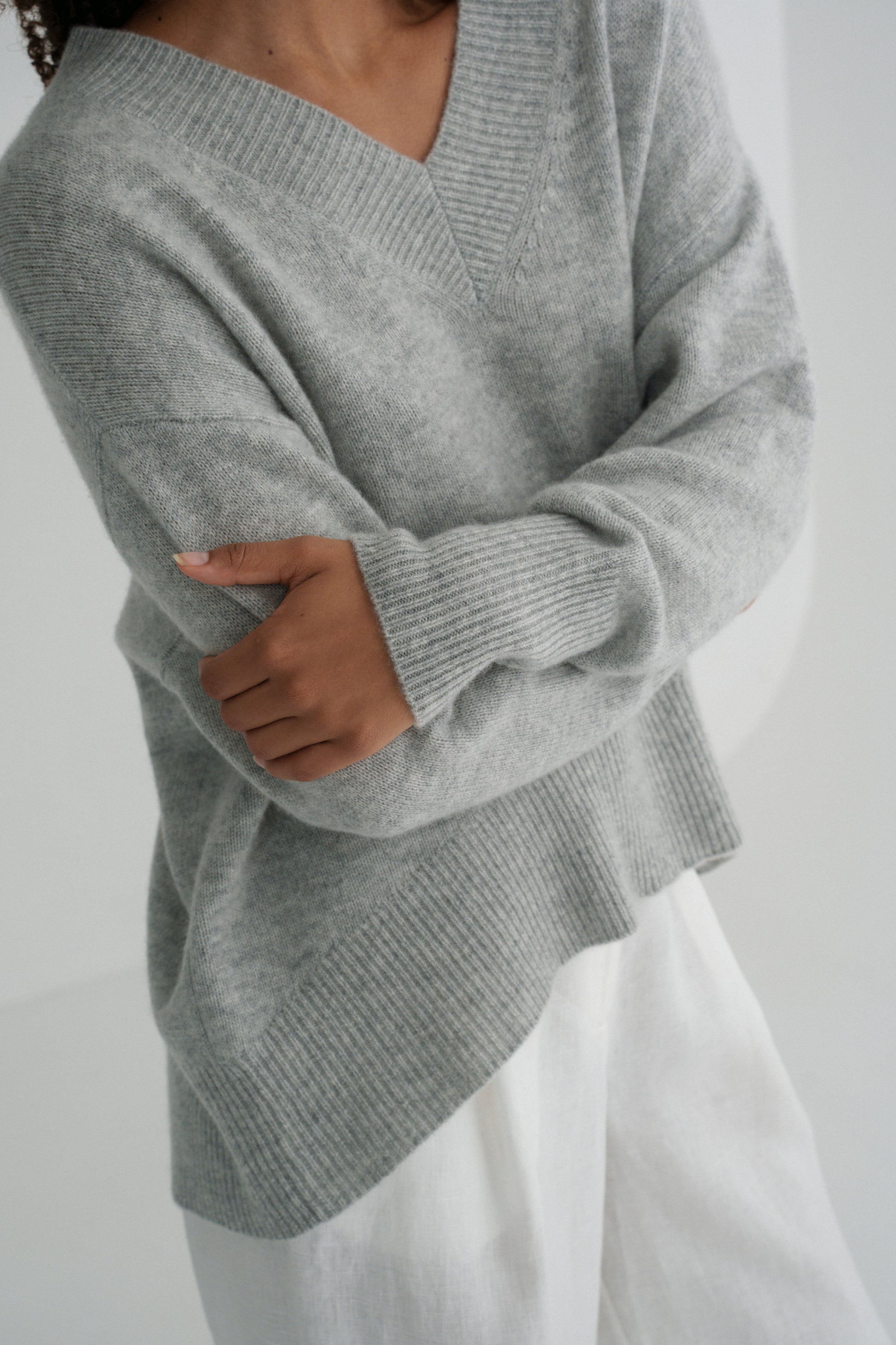Close up view of LILLY PILLY woman wearing a grey marle June cashmere knit sweater and ivory linen pants with a plain white background