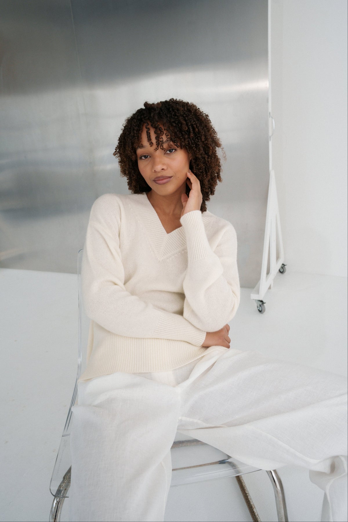 LILLY PILLY woman wearing an ivory June cashmere knit sweater sitting on a white couch.