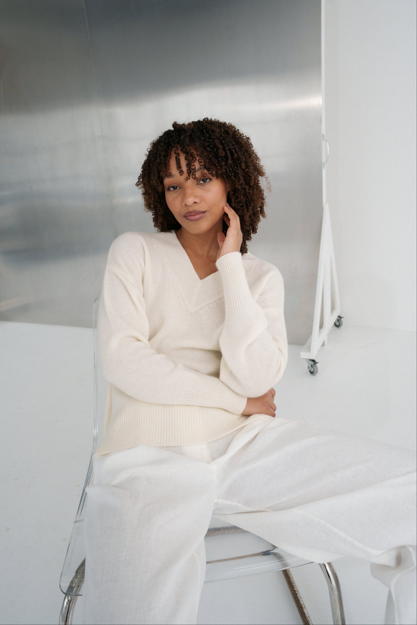 LILLY PILLY woman wearing an ivory June cashmere knit sweater sitting on a white couch.