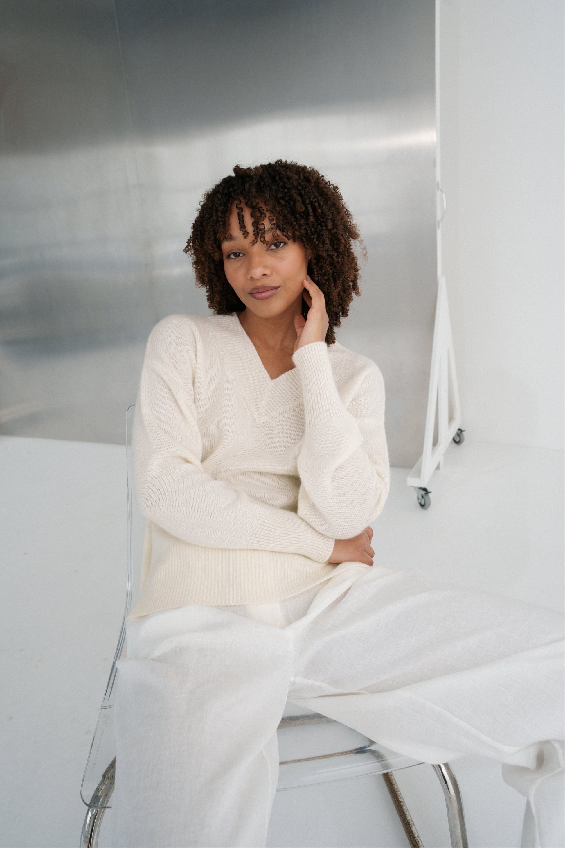 LILLY PILLY woman wearing an ivory June cashmere knit sweater sitting on a white couch.
