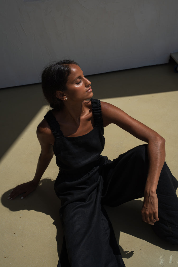 Seated woman wearing the Keely Linen jumpsuit in Black - Lilly Pilly Collection