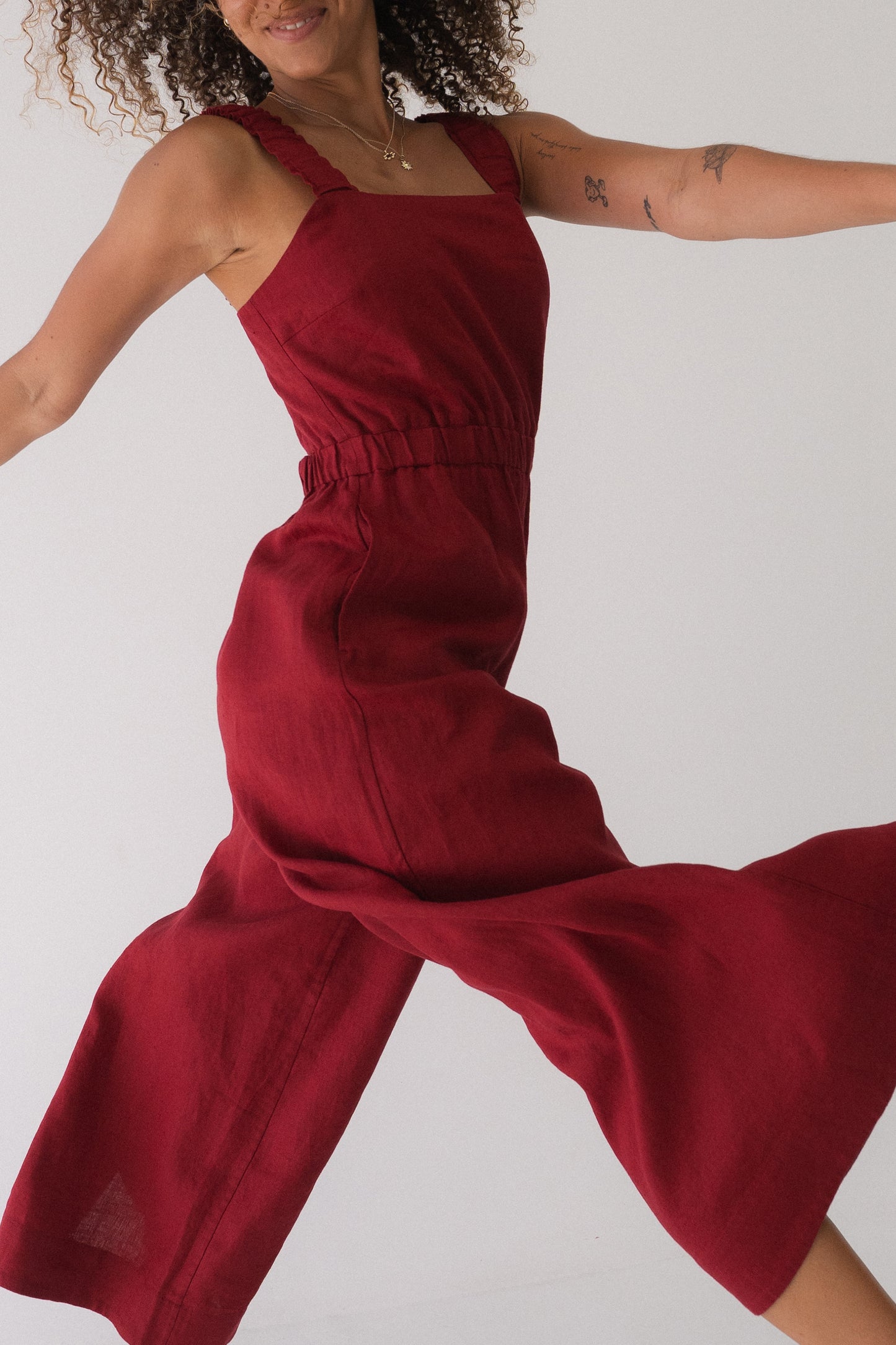 Close-up view of a woman wearing the Keely Linen jumpsuit in Cherry Red, mid- stride - Lilly Pilly Collection