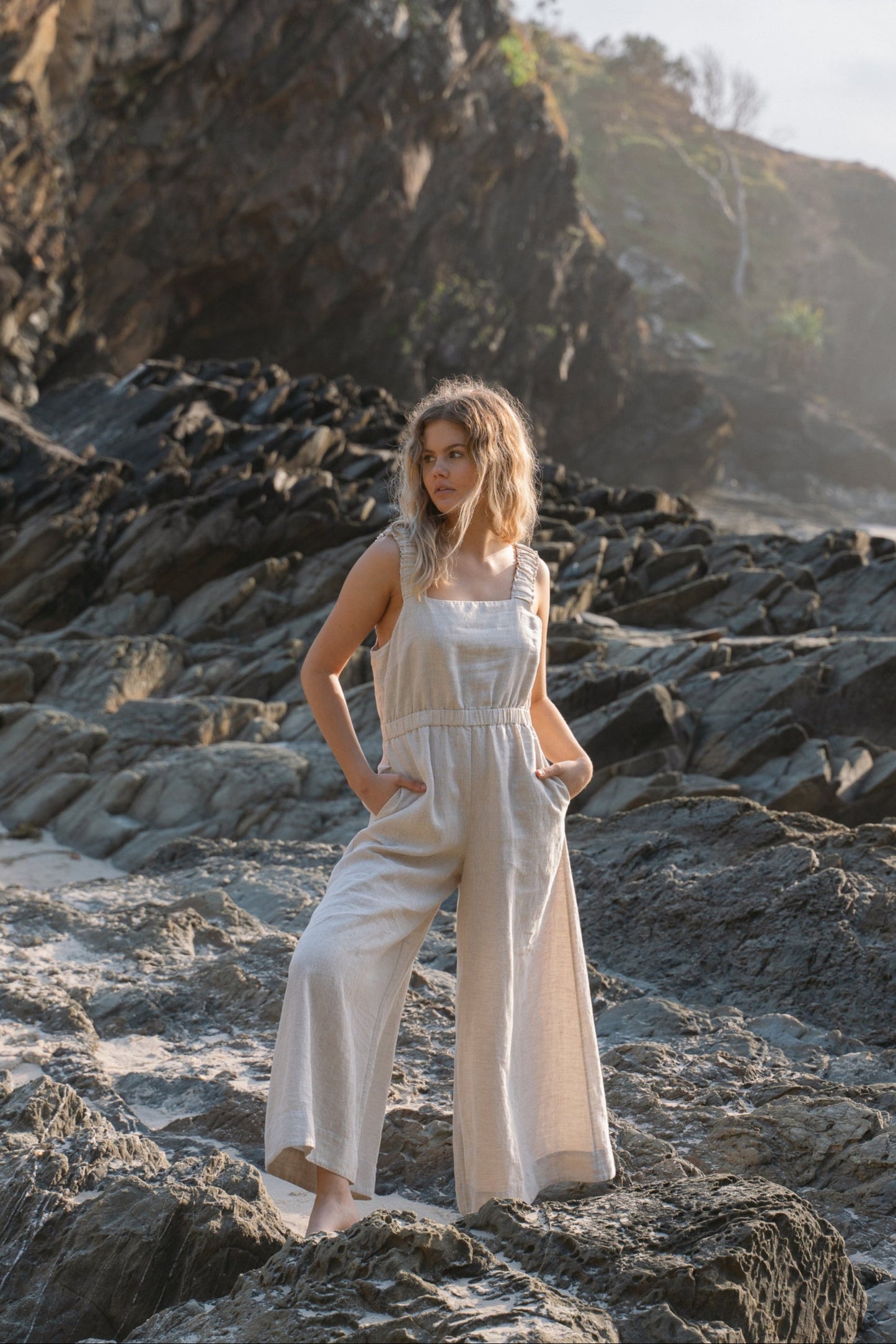 Woman wearing the Keely Linen jumpsuit in Oatmeal while on the rocks - Lilly Pilly Collection