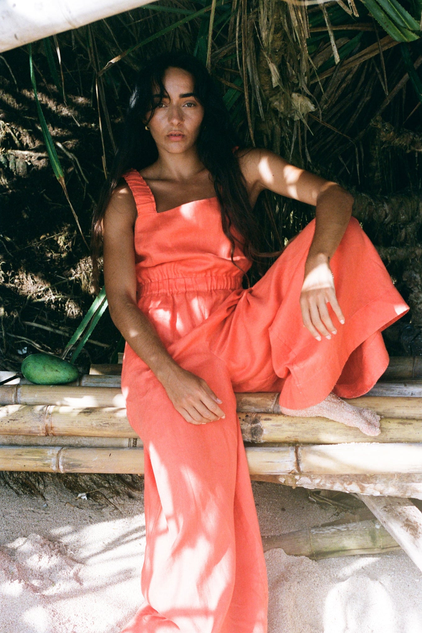 LILLY PILLY woman in an spritz Keely linen jumpsuit sitting on a bamboo structure with  greenery in the background