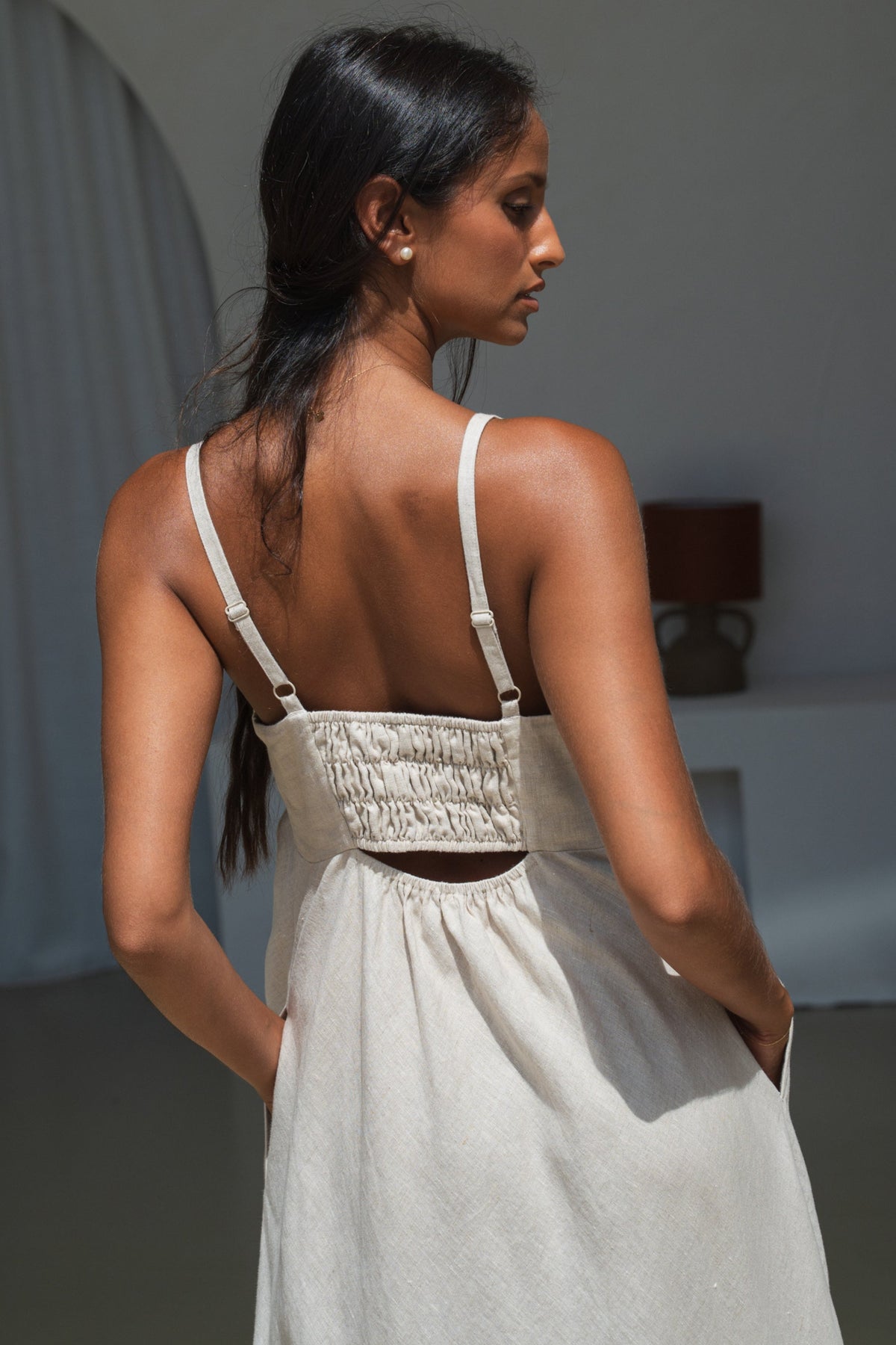 lilly pilly woman in an oatmeal Kiko linen dress showing back view while standing in a minimal indoor setting