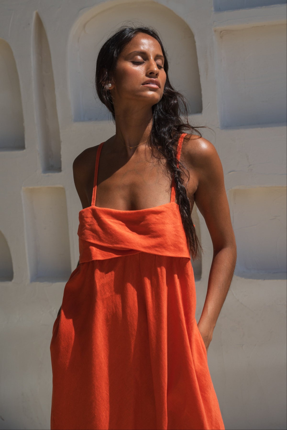 close up view of lilly pilly woman in a spritz coloured Kiko linen dress standing against a white wall with arches.