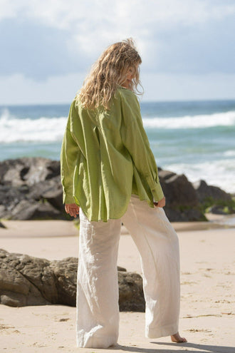 Kirra Linen Shirt in Lemongrass - back view, walking on beach with ocean backdrop, worn with Oli Linen Pants in Ivory - Lilly Pilly Collection