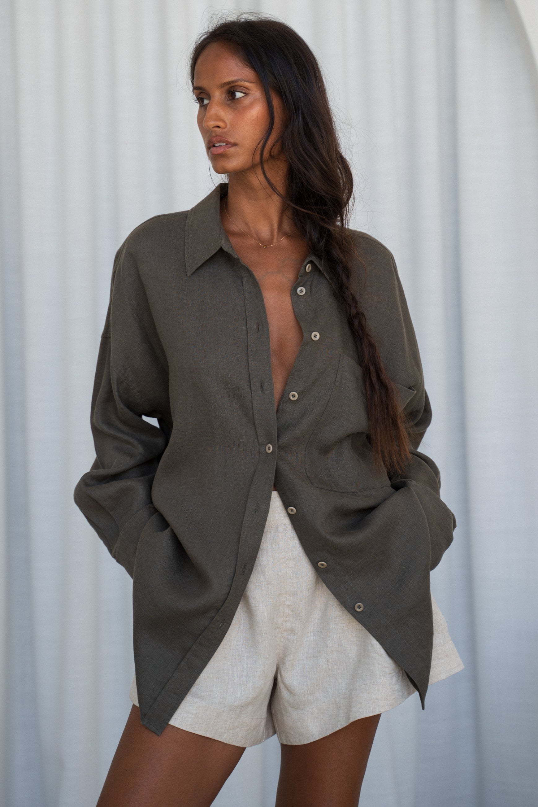 LILY PILLY woman wearing a khaki Kirra linen shirt with oatmeal shorts against a white curtain background
