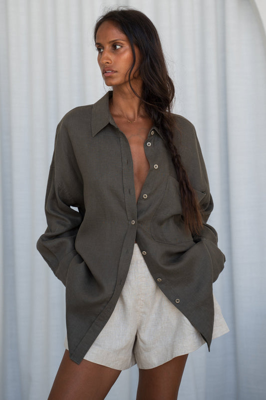 LILY PILLY woman wearing a khaki Kirra linen shirt with oatmeal shorts against a white curtain background