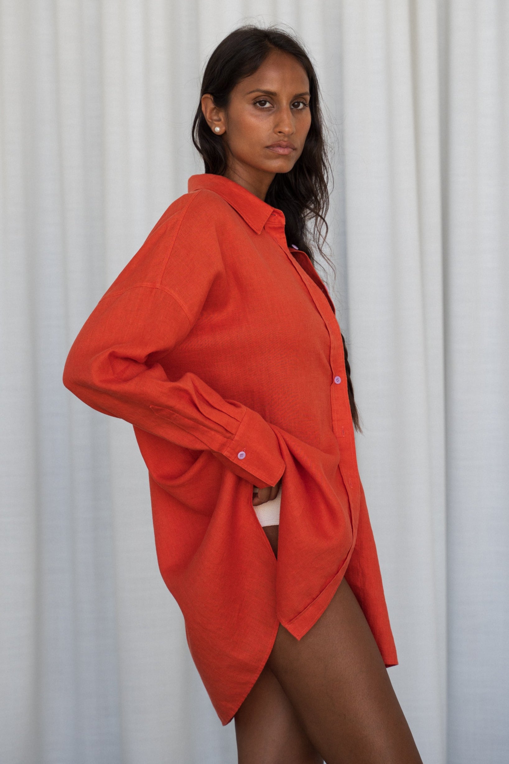 LILLY PILLY woman wearing a spritz Kirra linen shirt leaning against a  white curtain background