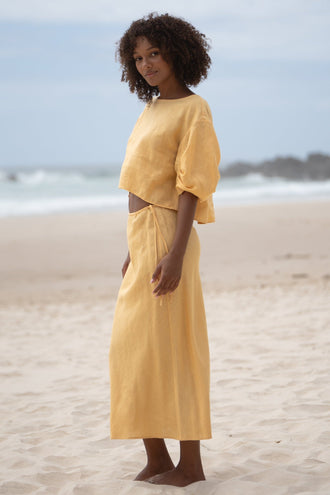 Leia Linen Top in Butter Yellow - side profile, boat neckline and cropped hem, worn with Riley Bias Linen Midi Skirt in Butter Yellow, standing on beach - Lilly Pilly Collection