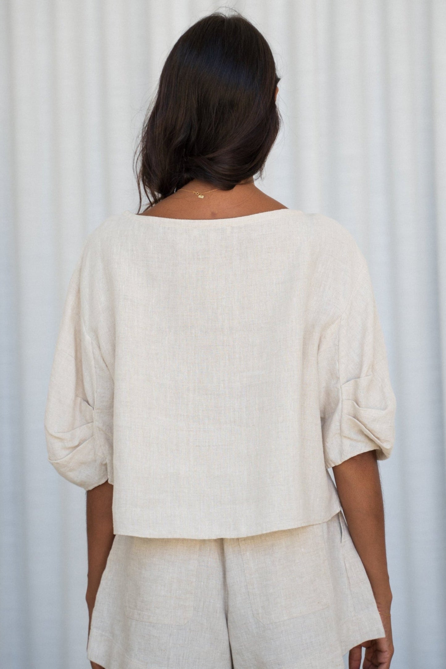 Woman wearing a oatmeal Leia linen top showing back view against a light gray background