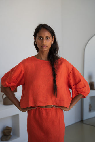 Leia Linen Top in Spritz Orange - front view, hands on hips, round neckline and puff sleeves, worn with matching pants, studio setting - Lilly Pilly Collection