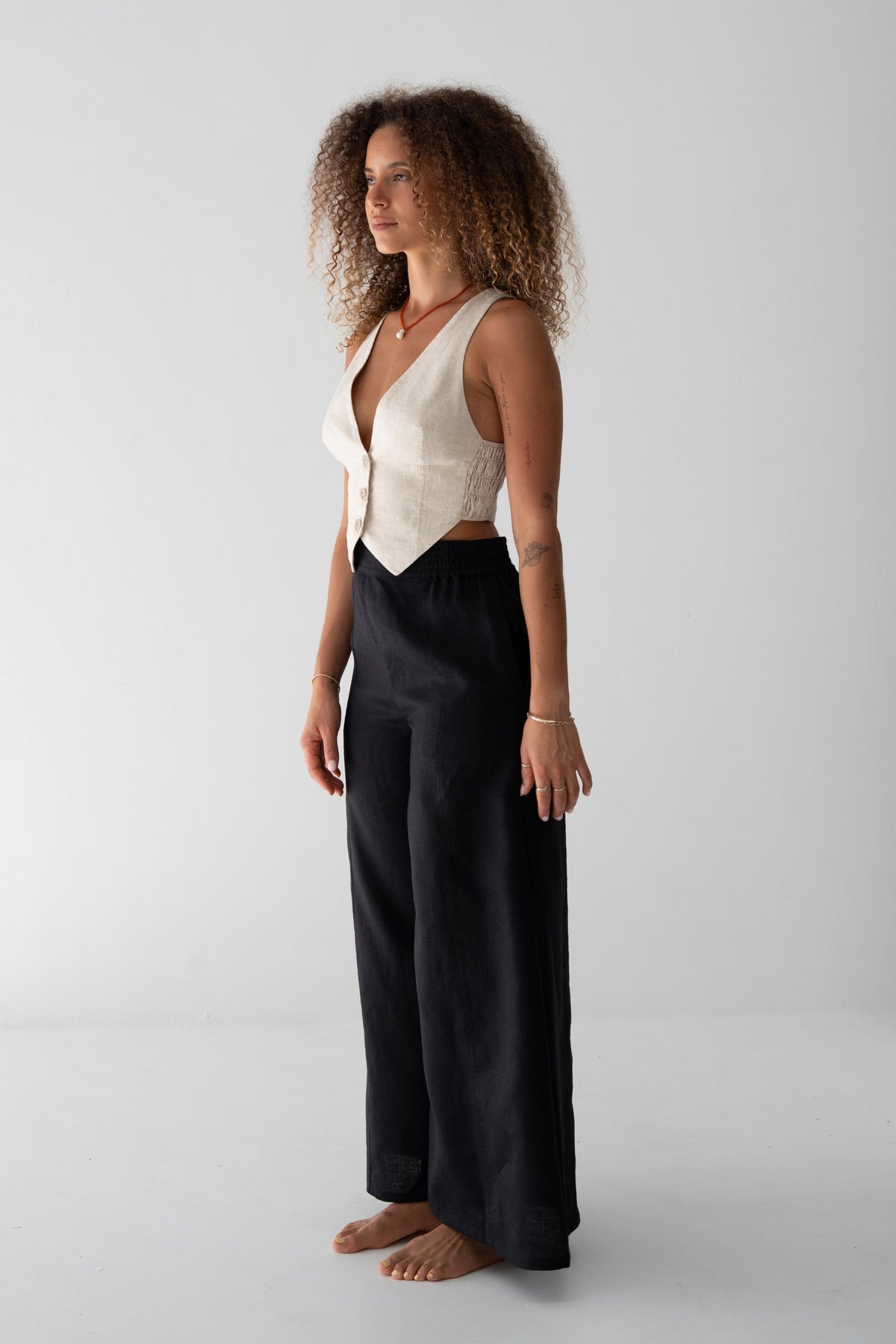 Letty Linen Pants in Black - side view, woman wearing Black wide-leg linen pants with ivory linen waistcoat, studio backdrop - Lilly Pilly Collection