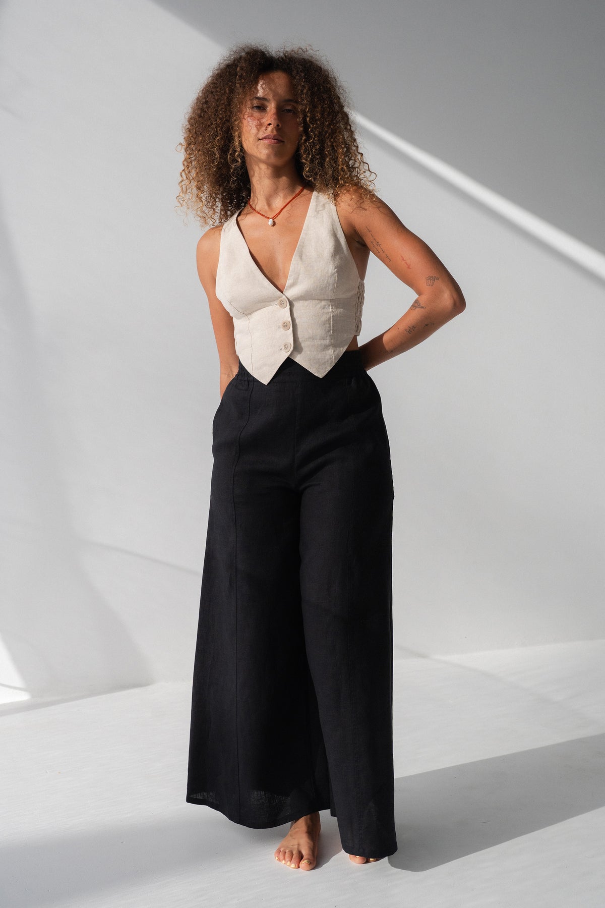 Letty Linen Pants in Black - full length front view, woman wearing Black wide-leg linen pants with ivory linen waistcoat, studio backdrop - Lilly Pilly Collection