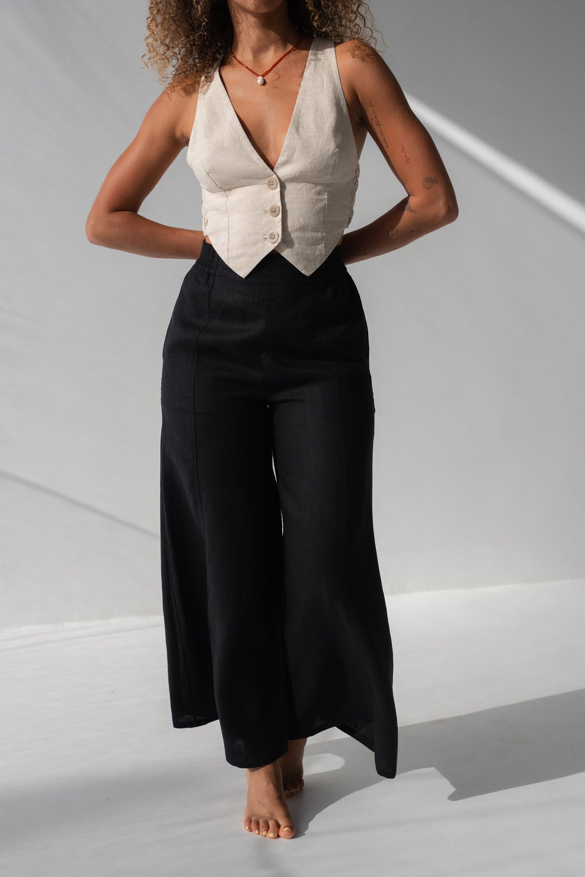 Letty Linen Pants in Black - close-up of high-waist wide-leg linen silhouette, woman wearing ivory linen waistcoat, studio backdrop - Lilly Pilly Collection