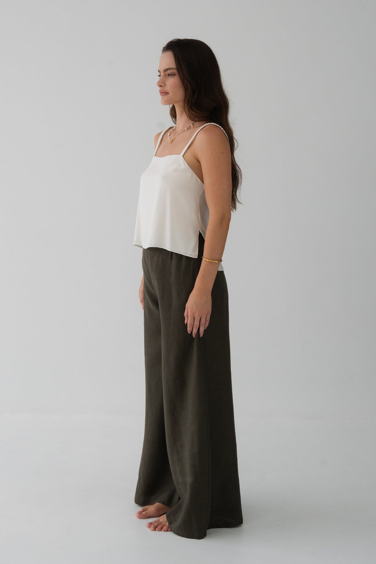 Letty Linen Pants in Khaki - side view, woman wearing Khaki wide-leg linen pants with ivory silk cami, studio backdrop - Lilly Pilly Collection