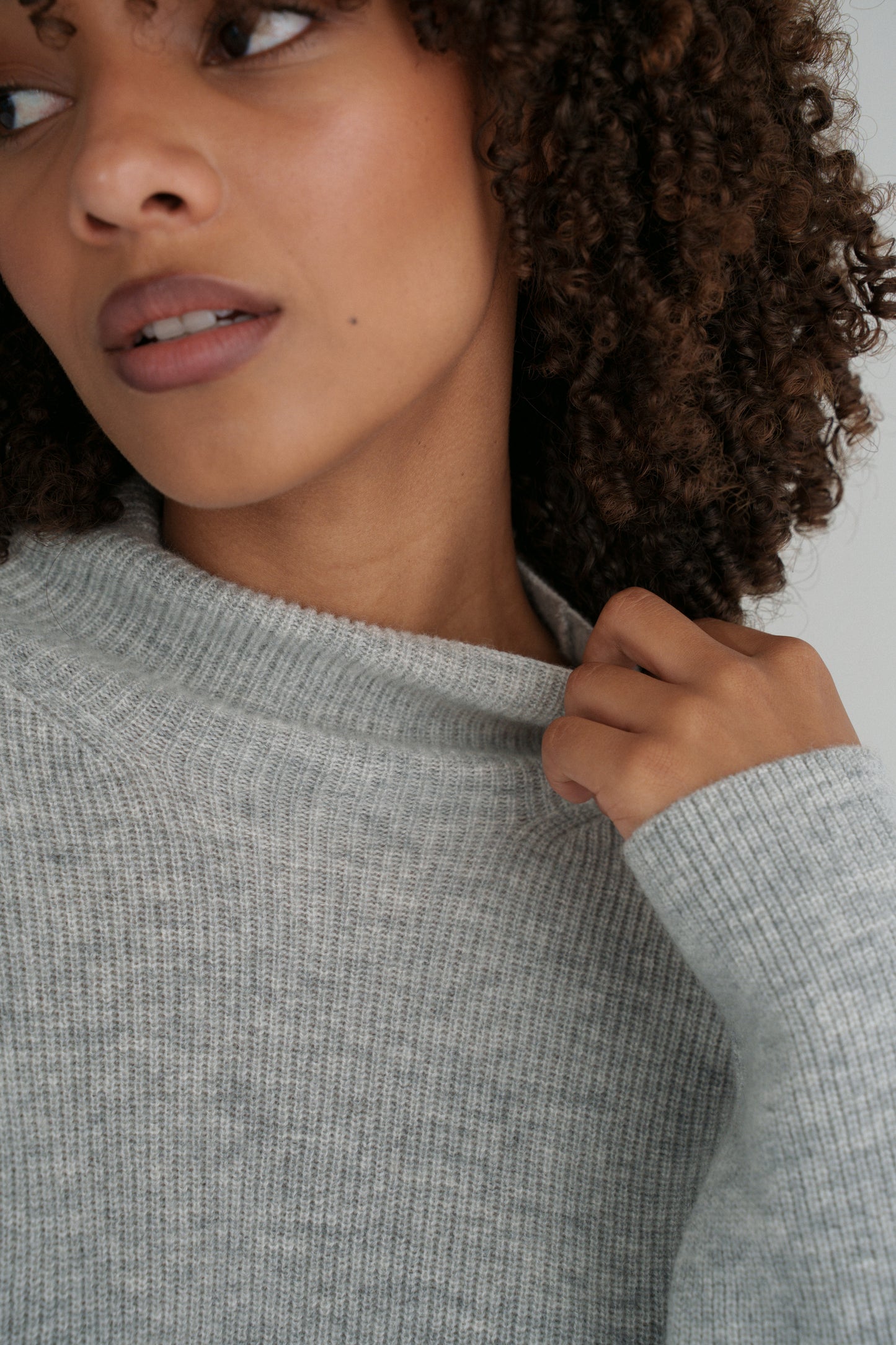 Close up of LILLY PILLY woman wearing a grey Lumi cashmere knit sweater and ivory white Gia skirt against a neutral background while holding collar