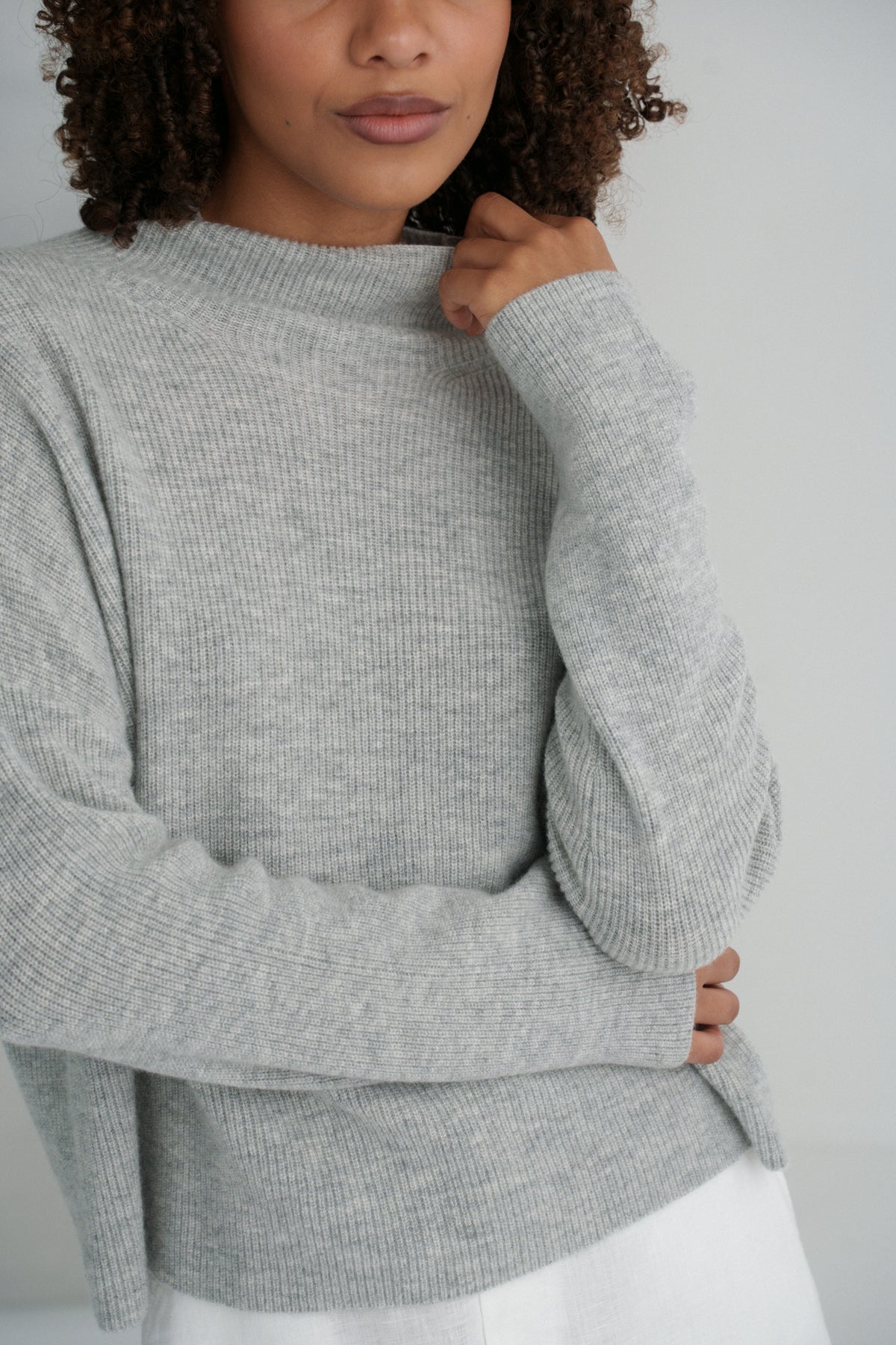 Close up front view of LILLY PILLY woman wearing a grey Lumi cashmere knit sweater and white Gia skirt against a white background