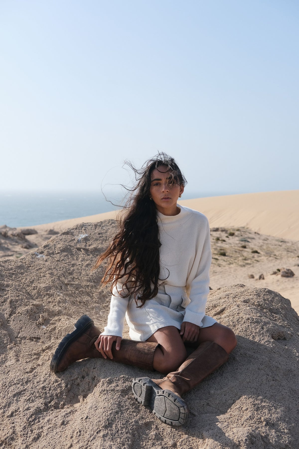 LILLY PILLY Lumi cashmere knit in Ivory sitting on a sandy beach with ocean and sky in the background